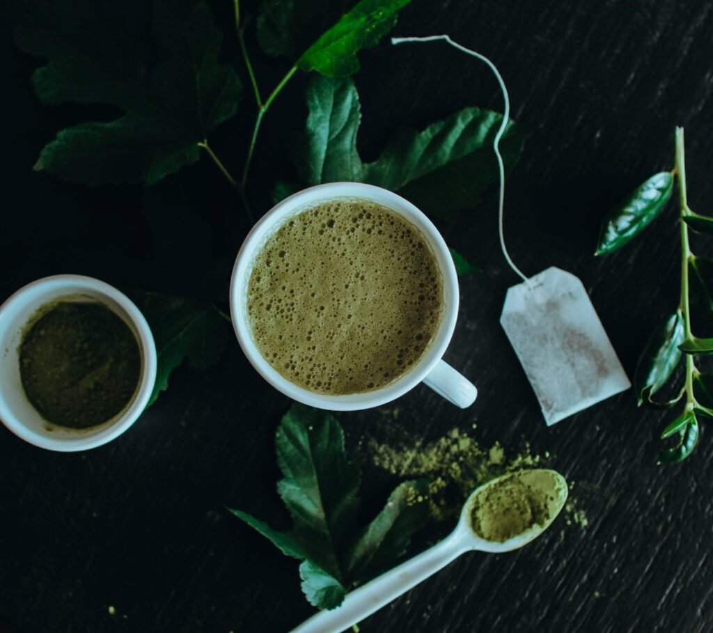 pexels-photo-5168515-5168515 Top view of a refreshing matcha latte surrounded by leaves, powder, and a tea bag.