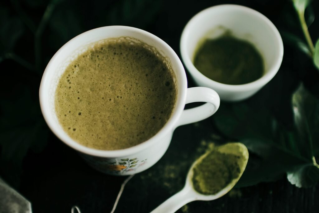 Close-up of a frothy matcha latte in a ceramic cup with matcha powder on spoon.